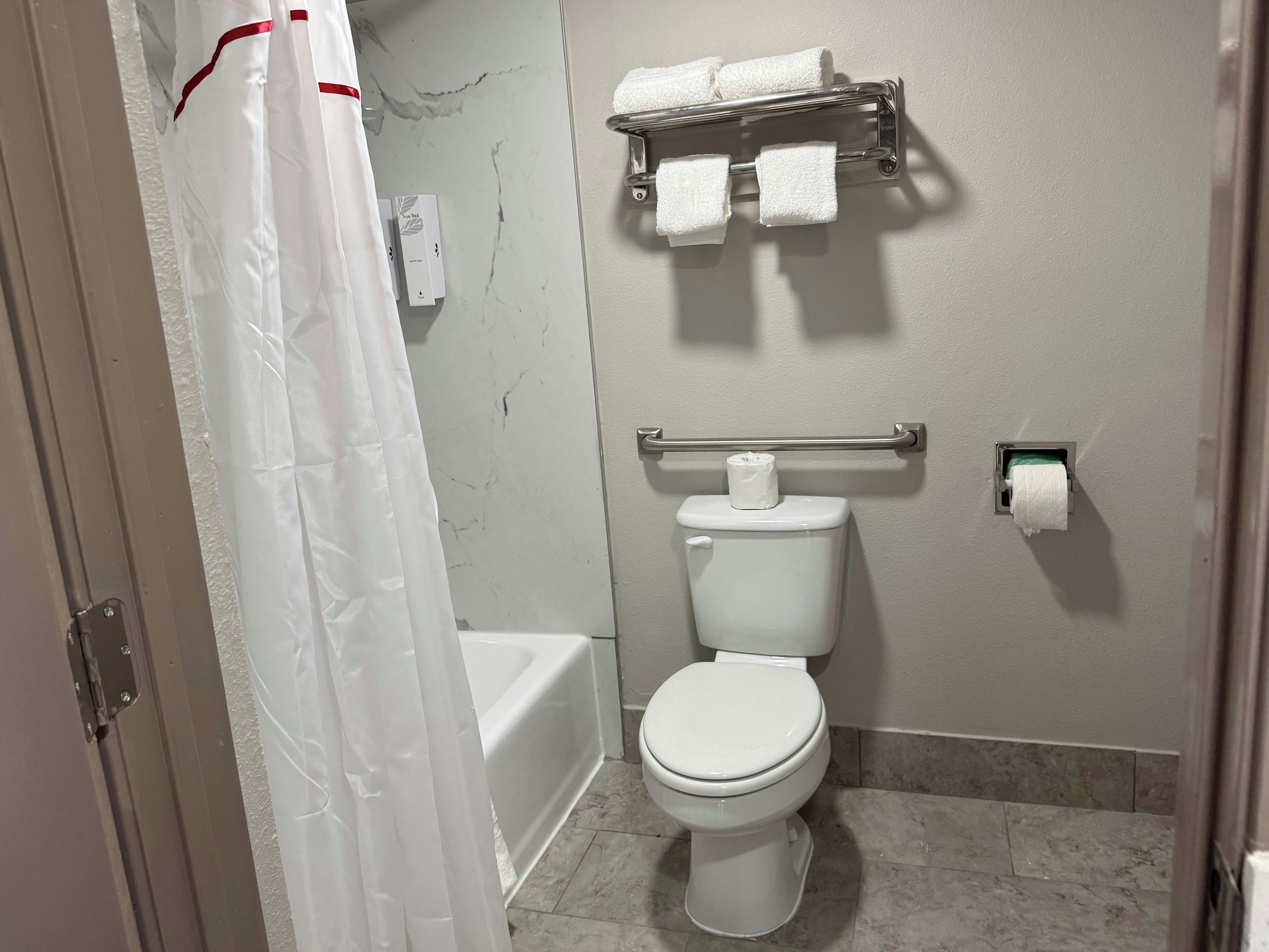A bathroom with a toilet, a towel rack with towels, a shower curtain, and a toilet paper holder.