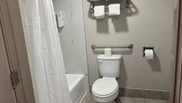 A bathroom with a toilet, a towel rack with towels, a shower curtain, and a toilet paper holder.