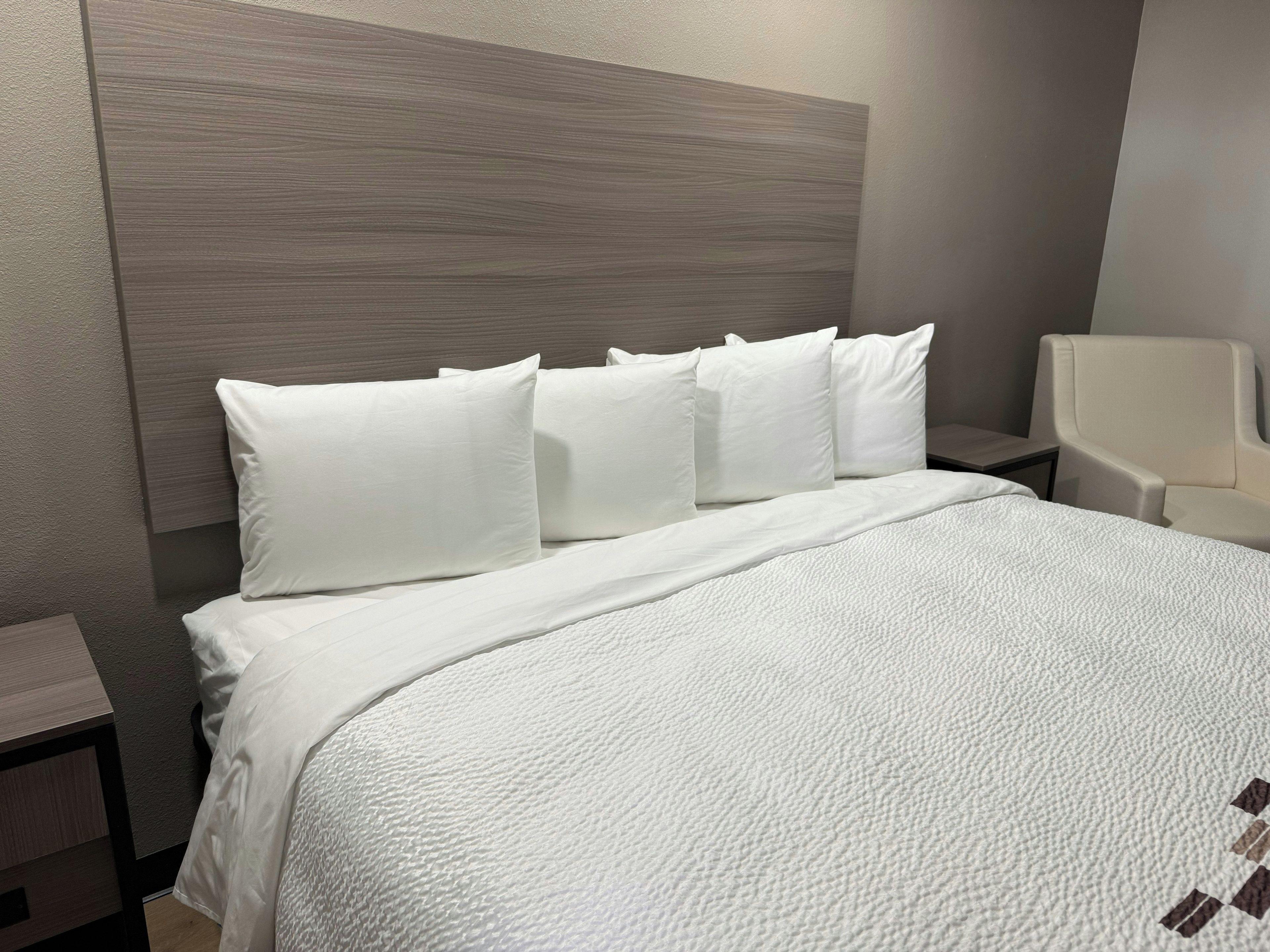 A hotel room with a bed, white bedding, a headboard, and a nightstand.