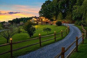 Ein großes, helles Chalet mit Kiesweg und Holzzaun, umgeben von üppigem Grün und Bäumen.