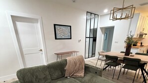 Un salon avec un canapé vert, une table à manger avec des chaises, un coin cuisine et une porte blanche.
