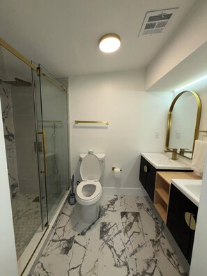 Een moderne badkamer met een douchecabine van glas, een toilet, een wastafel en een spiegel.