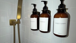 Une salle de bain avec une douche, deux bouteilles de shampoing et une bouteille d’après-shampoing.