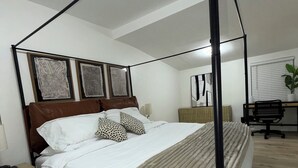 Une chambre à coucher avec un lit à baldaquin, un bureau avec une chaise, une plante en pot et des œuvres d’art accrochées au mur.