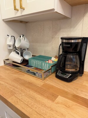 Een keukentafel met een koffiezetapparaat, een koffiebar en witte mokken.