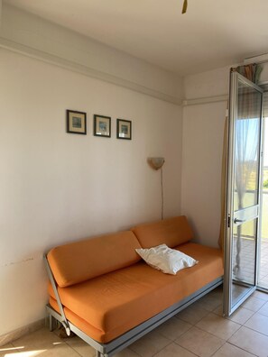 A room with a sofa, a wall-mounted lamp, and a door leading outside. - Ca Festa Residence: Two-room apartment Ca Festa 51 for 6 people (Chioggia)