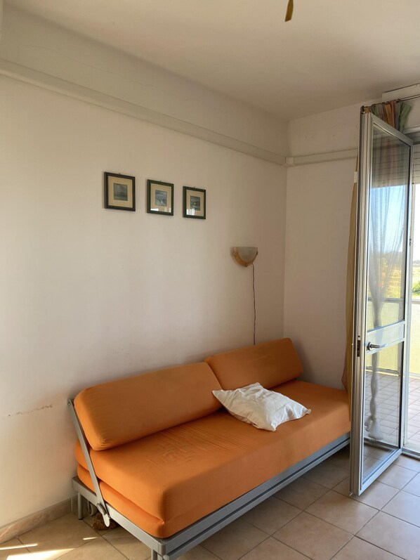 A room with a sofa, a wall-mounted lamp, and a door leading outside. - Ca Festa Residence: Two-room apartment Ca Festa 51 for 6 people (Chioggia)