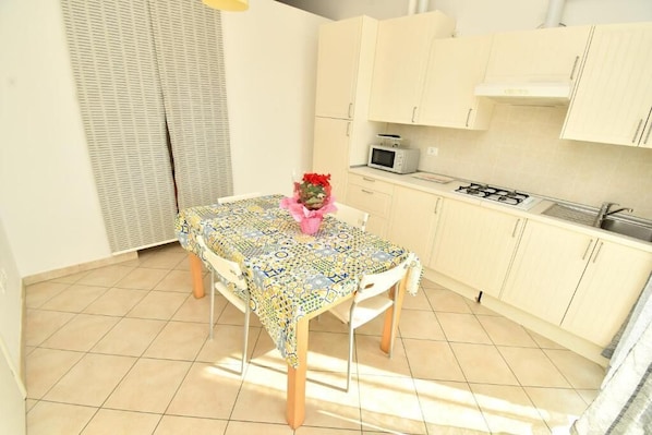 A small kitchen with a dining table, a microwave, and a gas stove. - Residenz Arcobaleno, Stella Marina 2 Two-Room Apartment for 4 People (Chioggia)