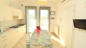 A kitchen with a tiled floor, a gas stove, cabinets, a dining table with a patterned tablecloth, and a TV mounted on the wall. - Residenz Arcobaleno, Stella Marina 2 Two-Room Apartment for 4 People (Chioggia)