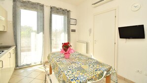 A room with a bed, a table with a patterned tablecloth, a TV on the wall, and a window with curtains. - Residenz Arcobaleno, Stella Marina 2 Two-Room Apartment for 4 People (Chioggia)