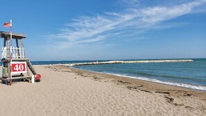 Ett livräddartorn med en röd flagga, en klarblå himmel och en sandstrand med en stenmur som vågbrytare i fjärran.