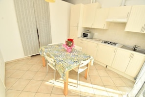 A small kitchen with a dining table, a microwave, and a gas stove. - Residenz Arcobaleno, Stella Marina 6 Two-Room Apartment for 4 People (Chioggia)