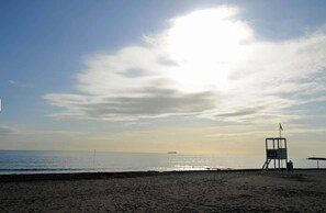 Ein Strand mit einem Rettungsturm, blauem Himmel und einem Schiff in der Ferne.