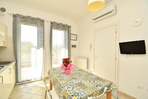Ein Zimmer mit einem Bett, einem Tisch mit gemustertem Tuch, einem an der Wand befestigten Fernseher und einem Fenster mit Vorhängen.