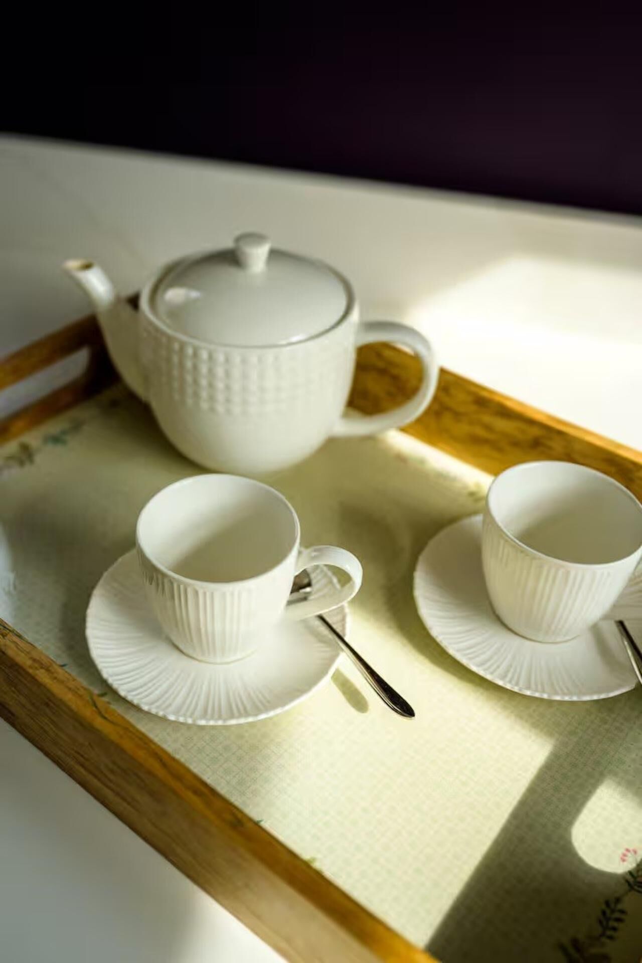 Un plateau avec une théière, deux tasses et une cuillère, posé sur une table.