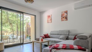Una sala de estar moderna con un sofá gris, una mesita y un amplio ventanal corredera que da a un espacio exterior.