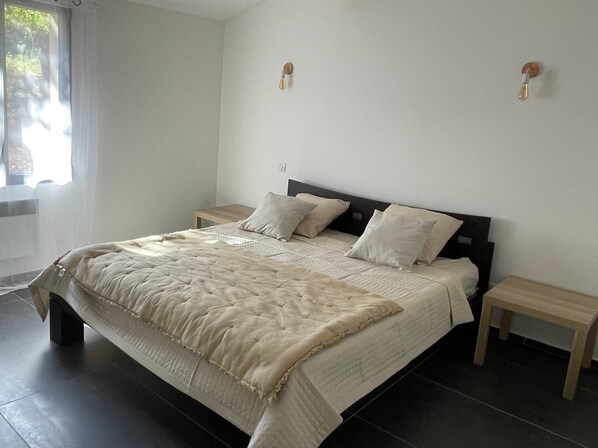 Een slaapkamer met een bed, twee nachtkastjes, een raam met gordijnen en een wandlamp.