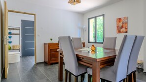Un comedor con una mesa de madera, sillas grises, una lámpara colgante y un ventanal con vistas a zonas verdes.