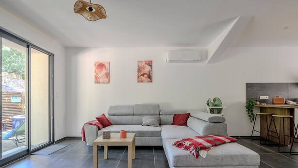 Un moderno salón con un sofá seccional gris, una pequeña mesa de madera y un gran ventanal corredizo que da a un área exterior.