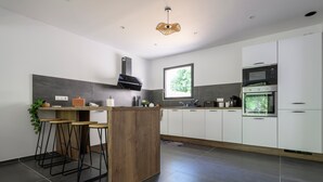 Una cocina moderna con una isla central, taburetes de bar, estufa integrada y un amplio ventanal.