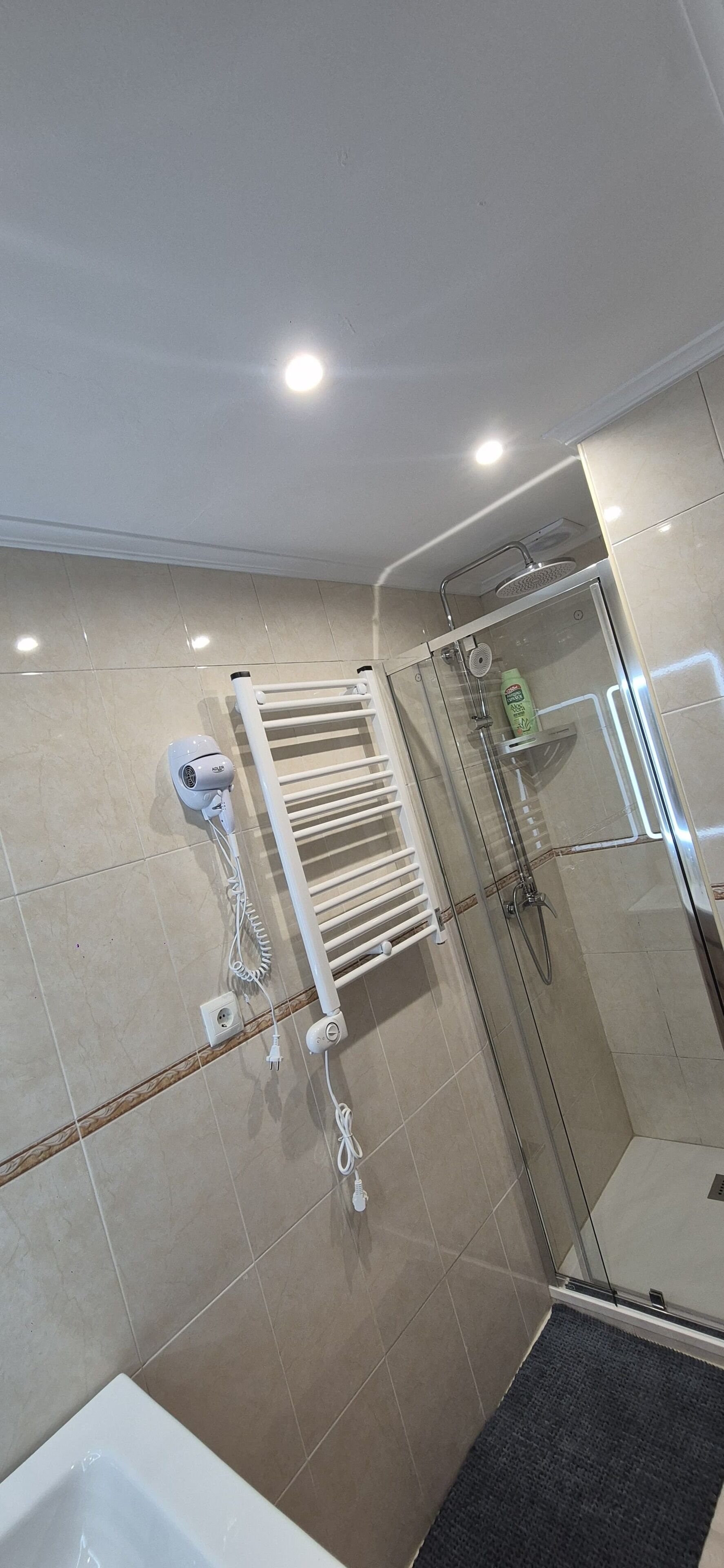 Un baño moderno con cabina de ducha de vidrio, un toallero blanco y un secador de pelo en la pared.