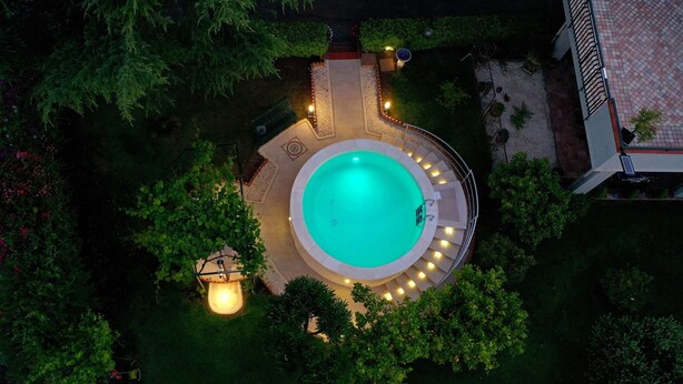 Ein kreisförmiger Pool, umgeben von einer gepflasterten Terrasse mit einem beleuchteten Weg, der von üppiger Vegetation gesäumt ist.