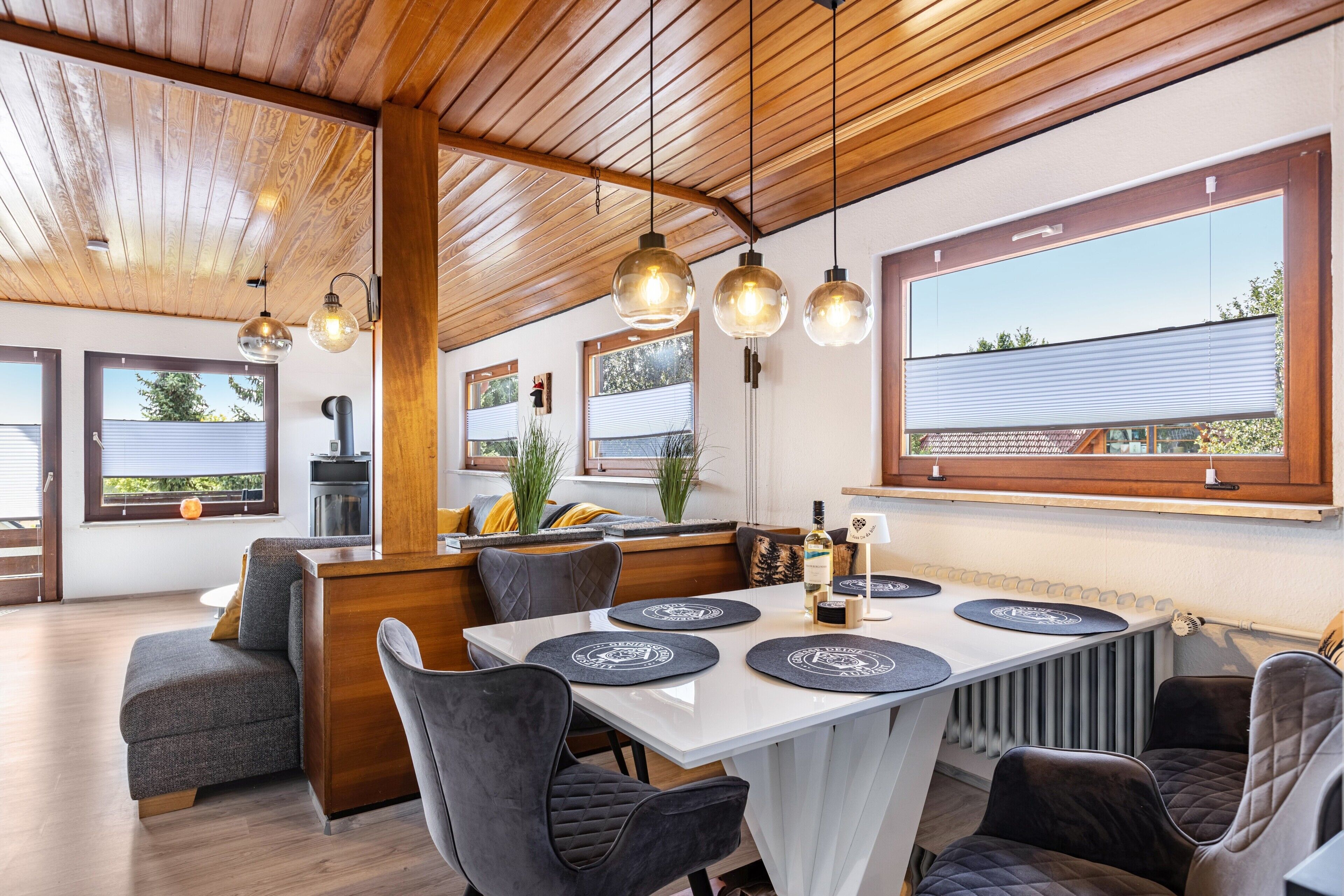 Een moderne eetruimte met een houten plafond, hanglampen en grote ramen met uitzicht op de omgeving.