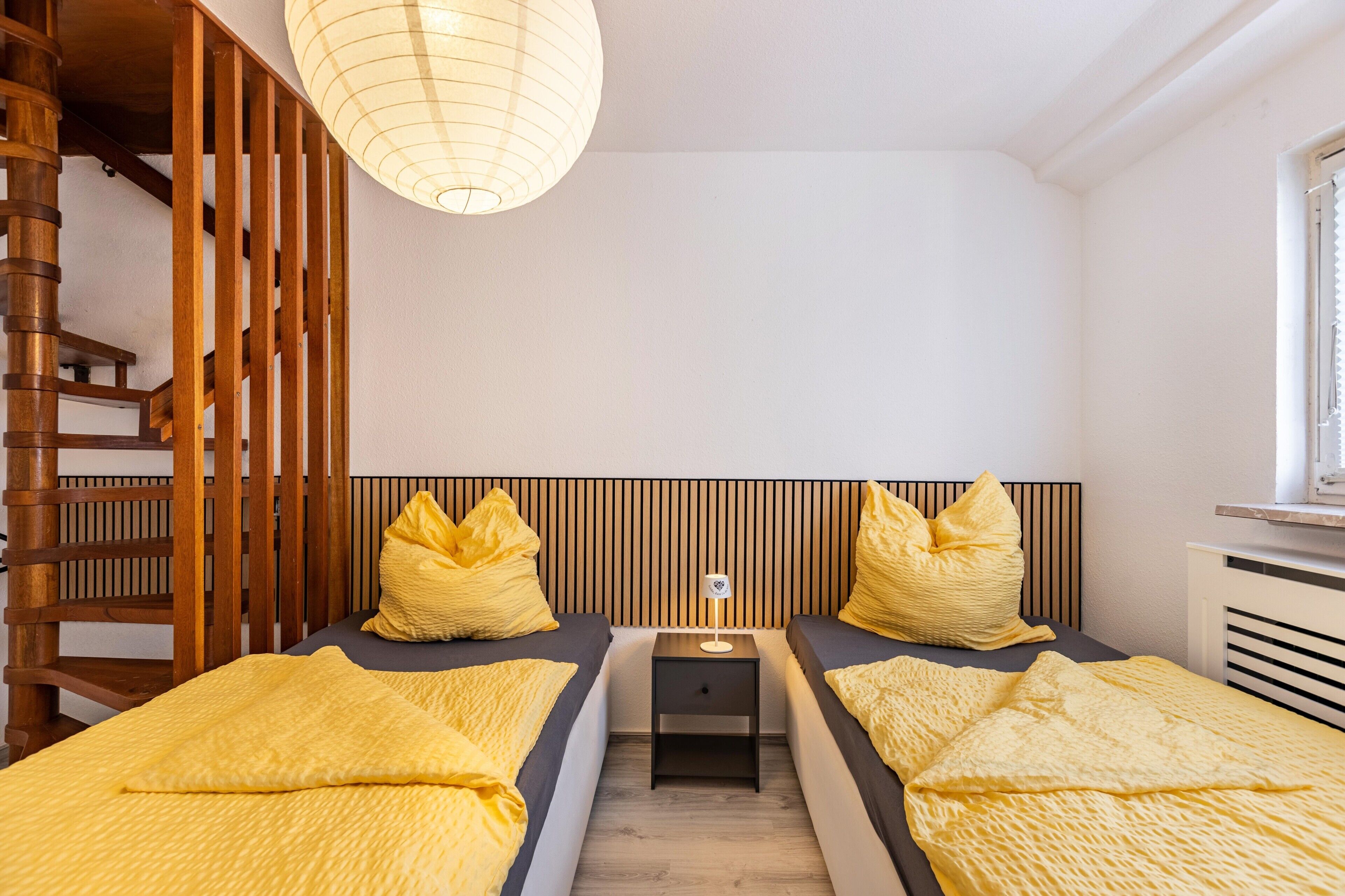 A bedroom with two beds, a nightstand, a lamp, and a window.
