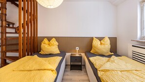 A bedroom with two beds, a nightstand, a lamp, and a window.