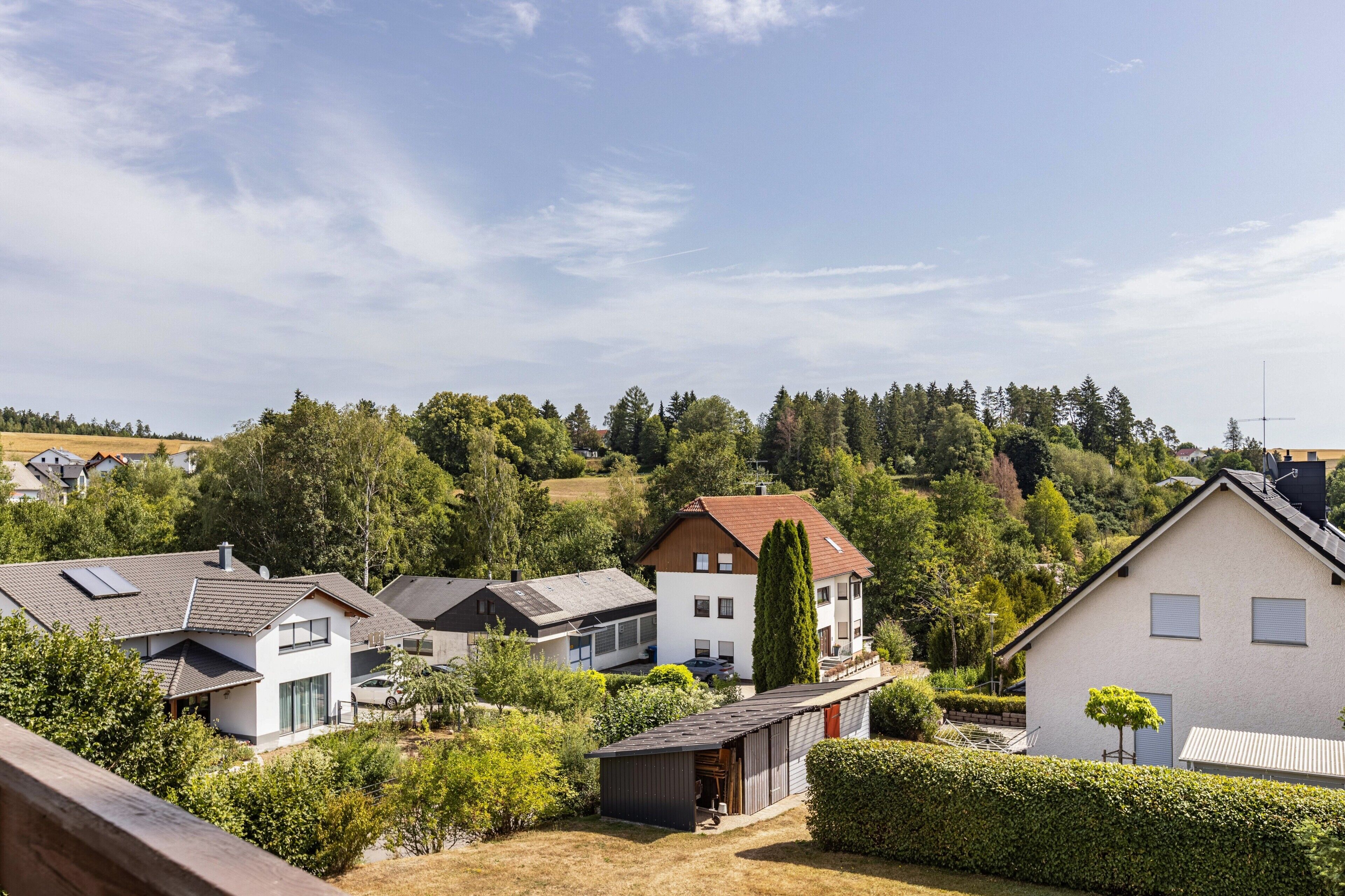 Een woonwijk met huizen, een heldere lucht en een heuvellandschap op de achtergrond.