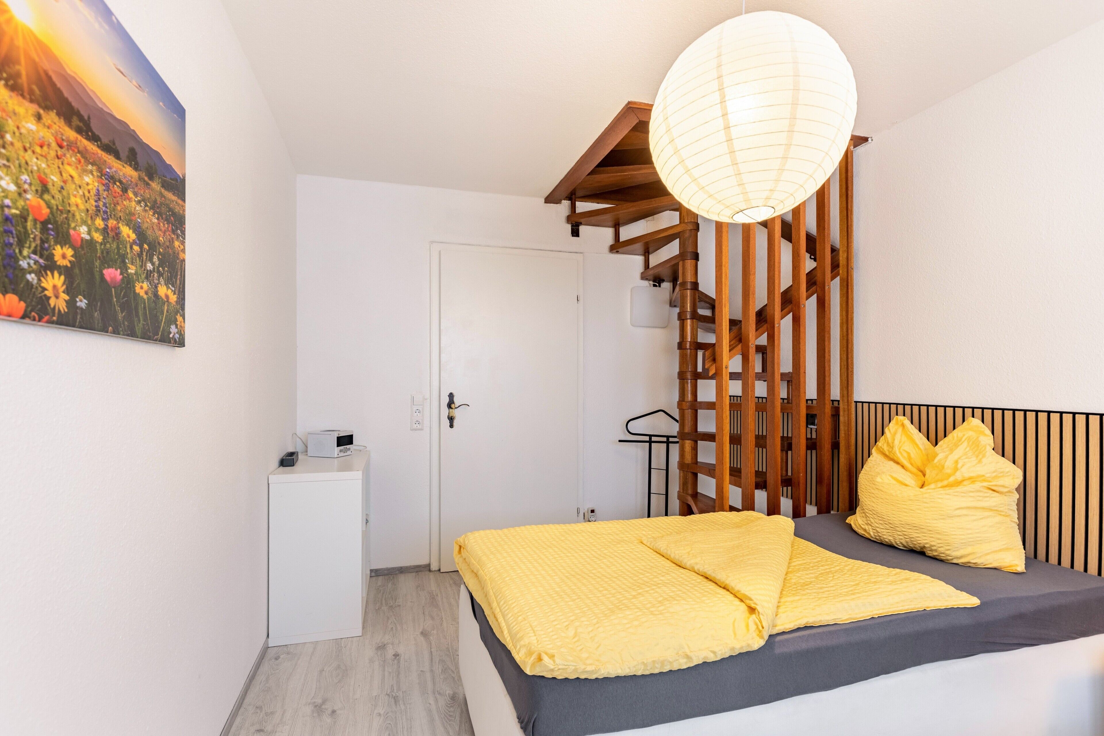 A bedroom with a bed, a bedside table, a lamp, and a painting on the wall.