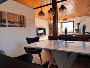 Una cocina moderna con una mesa de comedor de vidrio, lámparas colgantes y una obra de arte en la pared.