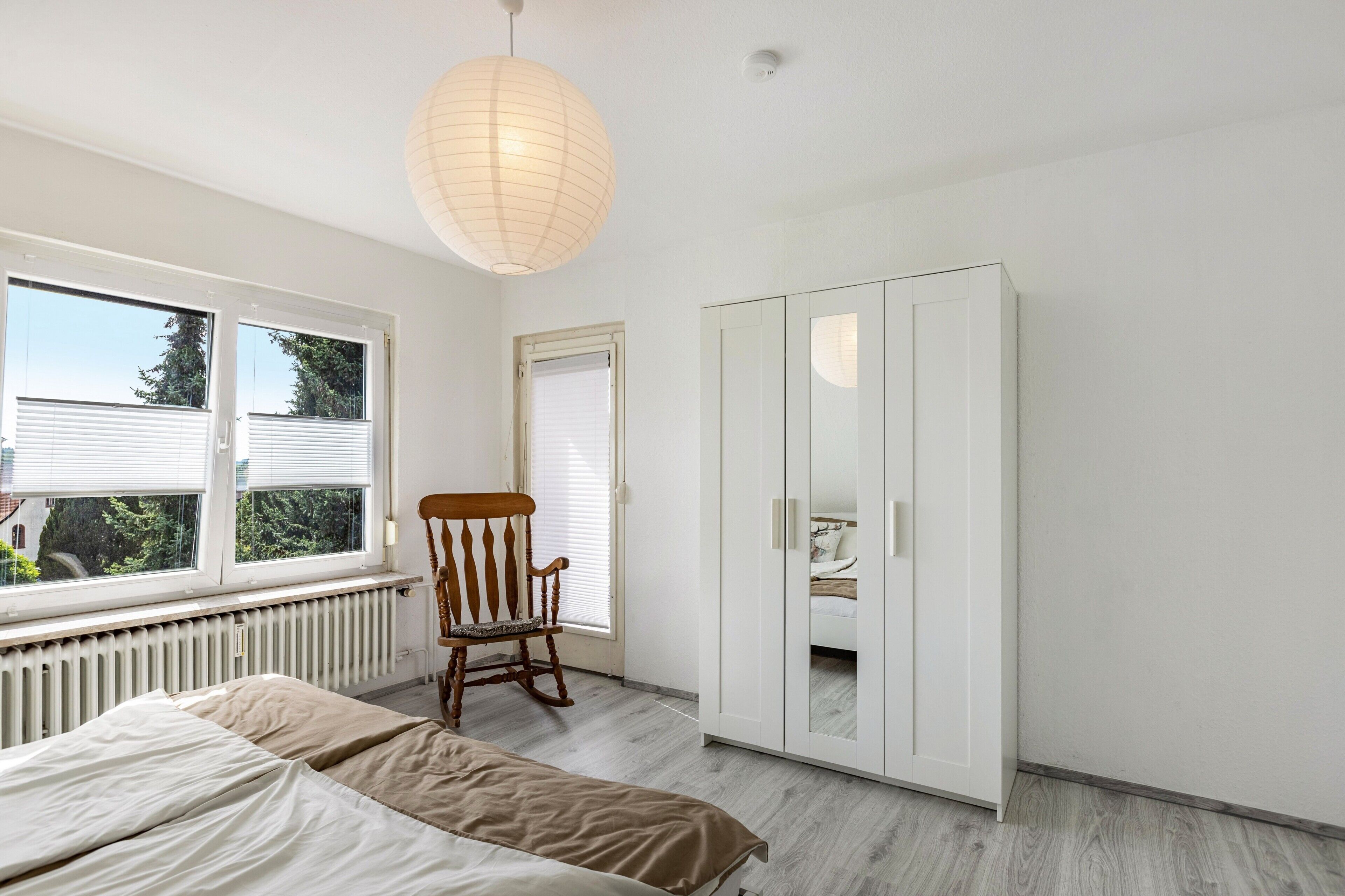 Ein Schlafzimmer mit einem Bett, einem Schaukelstuhl, einem Kleiderschrank und einem Fenster mit Jalousien.
