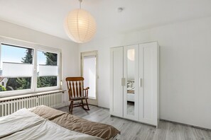 A bedroom with a bed, a rocking chair, a wardrobe, and a window with blinds.