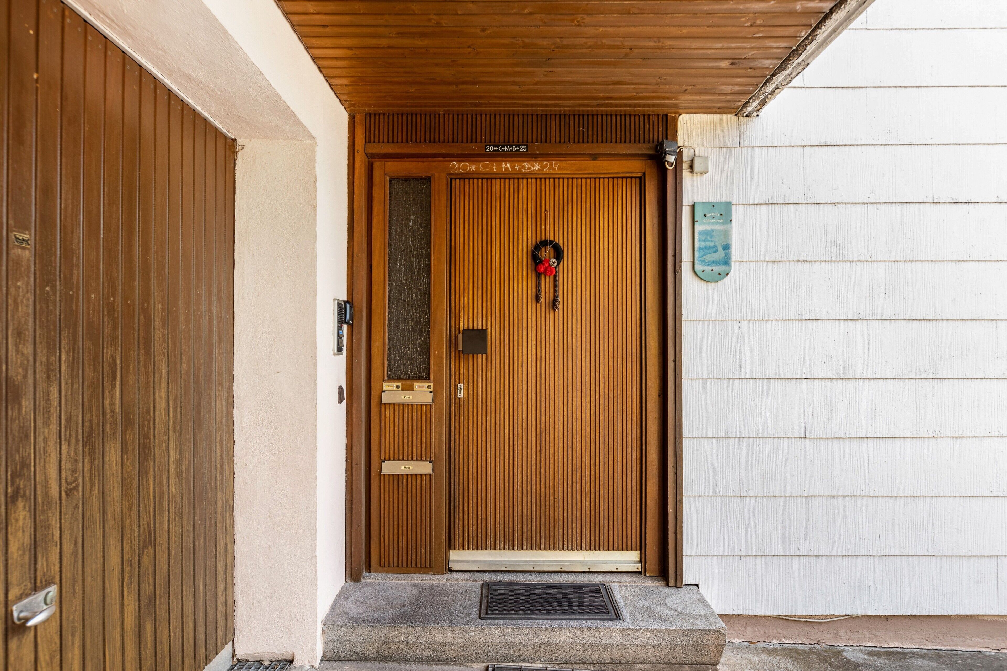 A wooden door with a glass panel and a wreath, leading to a stone-paved entrance.