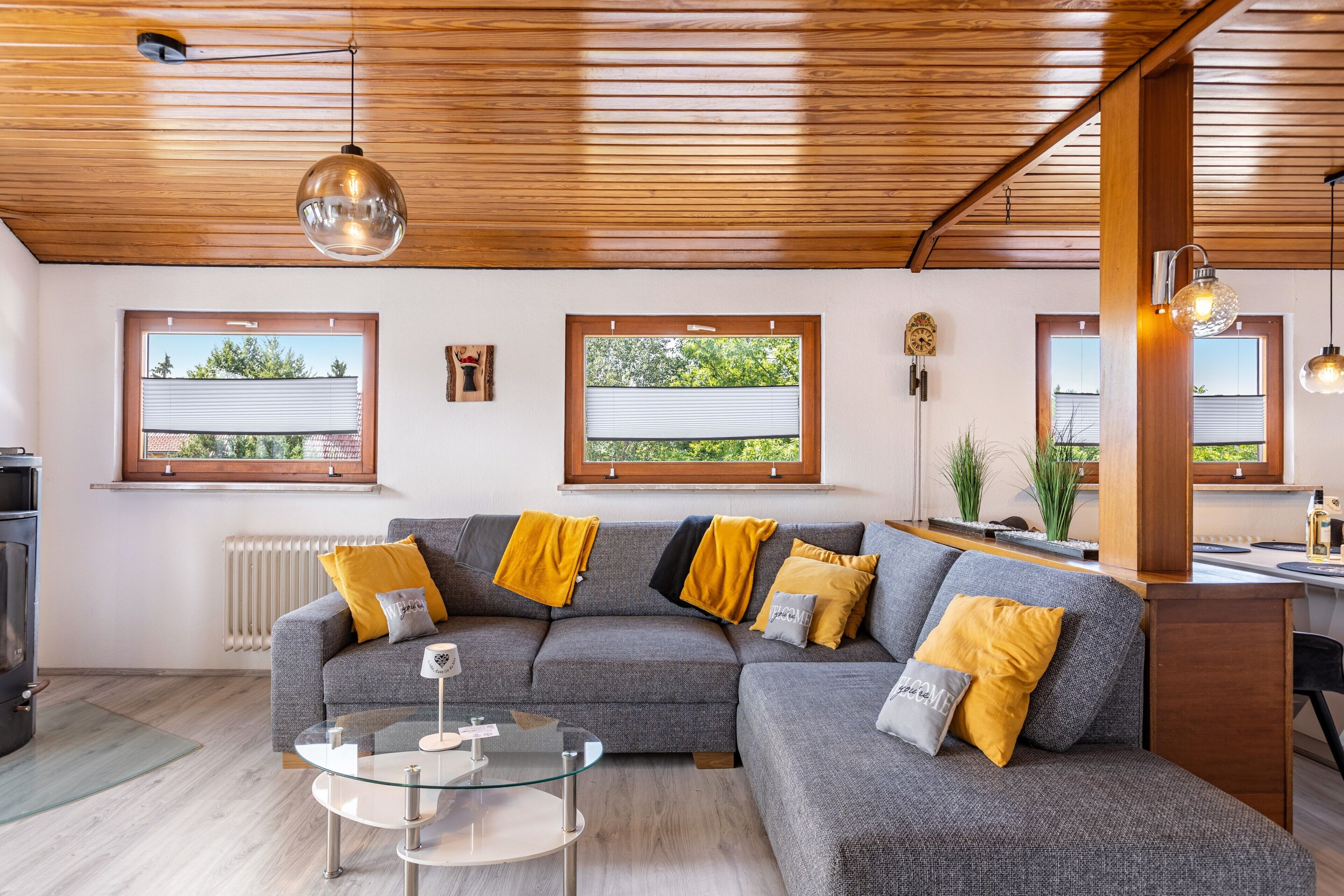 A modern living room with a sectional sofa, a glass coffee table, and a kitchen area with a stove.