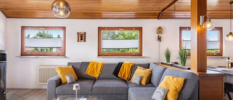 A modern living room with a sectional sofa, a glass coffee table, and a kitchen area with a stove.