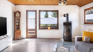 A living room with a wooden ceiling, a television, a clock, a glass coffee table, a sofa, and a fireplace.