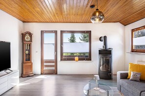 A living room with a wooden ceiling, a television, a clock, a glass coffee table, a sofa, and a fireplace.