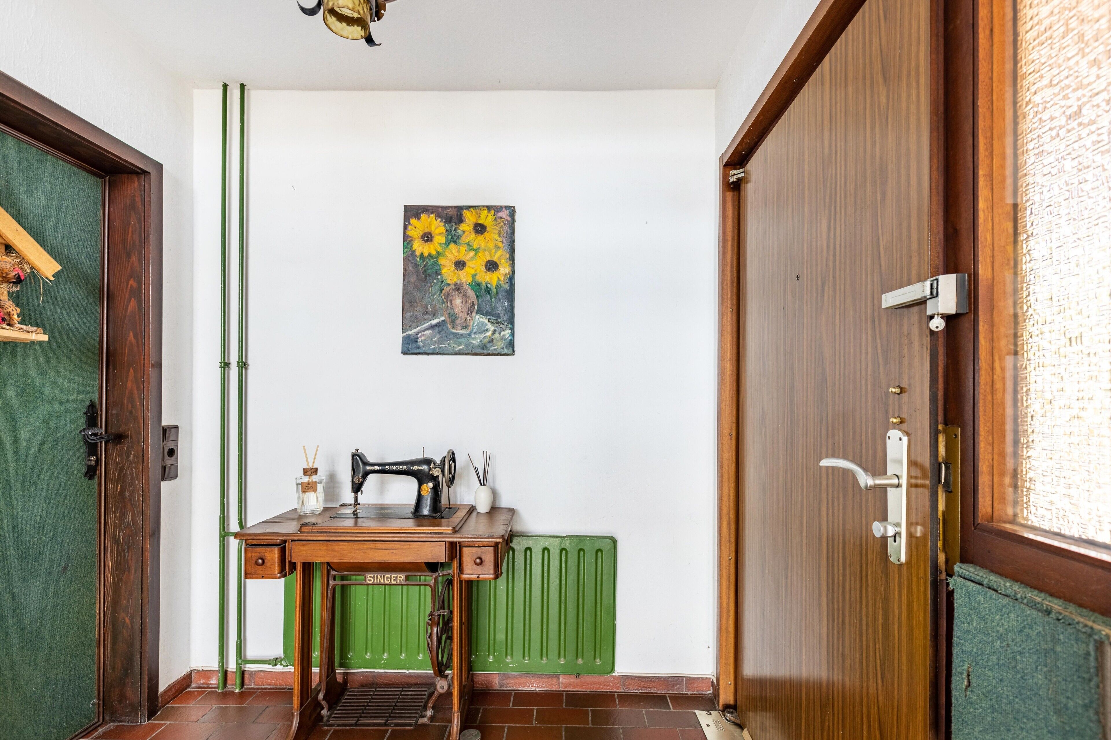 A room with a sewing machine, a radiator, and a painting of sunflowers on the wall.