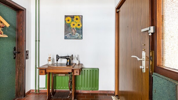 A room with a sewing machine, a radiator, and a painting of sunflowers on the wall.