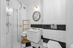 Kylpyhuoneessa on suihku, peilillä varustettu pesuallas, wc ja pieni puinen jakkara.