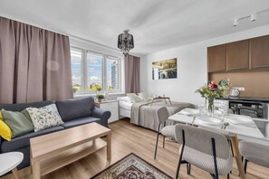 Moderni huoneisto, jossa on sohva, kahdelle katettu ruokapöytä, sänky ja keittiöalue.
