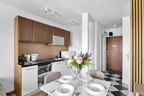 A modern kitchen with wooden cabinets, a dining area with a table set for two, and a door leading to another room. - Wola Studio - Train and Metro nearby -by Rentujemy (Warszawa)