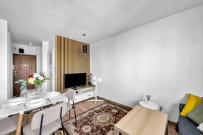 A modern living room with a dining area, a flat-screen TV, a fan, and a patterned rug. - Wola Studio - Train and Metro nearby -by Rentujemy (Warszawa)