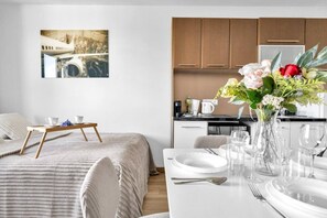A modern hotel room with a bed, bedside table, and a dining area with a table set for two. - Wola Studio - Train and Metro nearby -by Rentujemy (Warszawa)