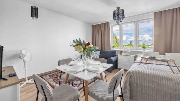 Ett modernt hotellrum med en matplats, en säng, ett skrivbord och ett stort fönster med utsikt över staden.