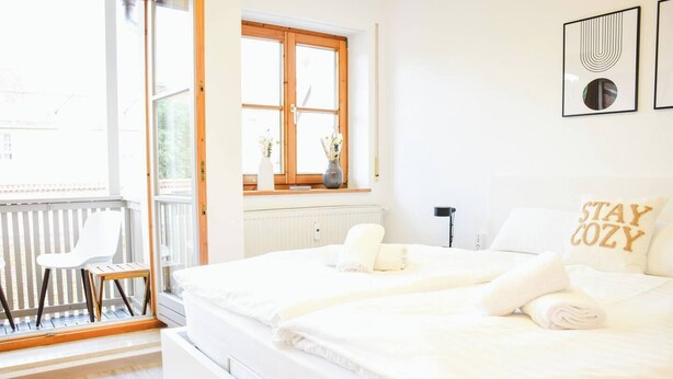 A bedroom with a large bed, a chair, a window, and a wall with framed artwork.