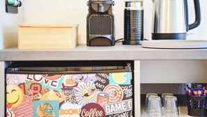 A kitchen counter with a coffee maker, a kettle, and a refrigerator with a colorful sticker design.