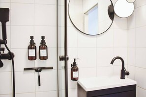 Een moderne badkamer met een witte wastafel, een ronde spiegel en twee flessen shampoo.